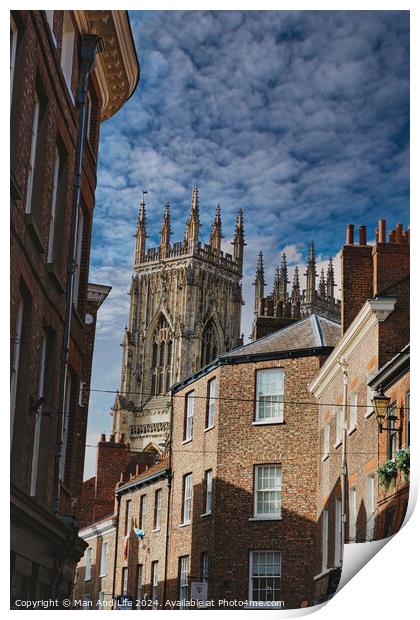Quaint cobbled street leading to a majestic Gothic cathedral under a blue sky with wispy clouds, showcasing historical architecture and urban charm in York, North Yorkshire, England. Print by Man And Life