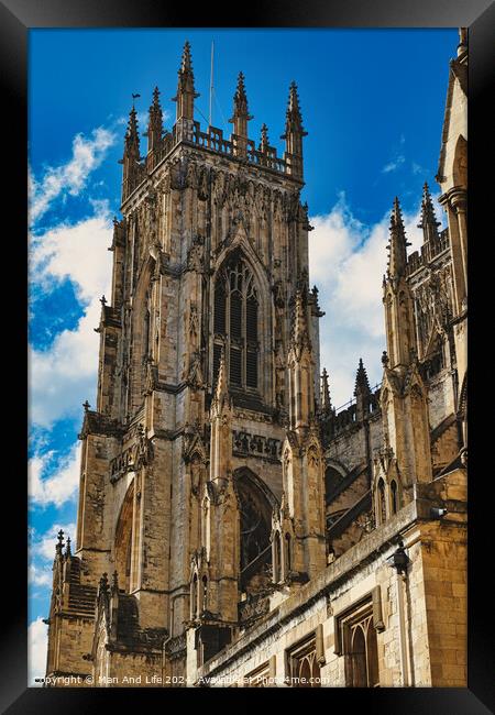 Gothic cathedral tower against a blue sky with clouds, showcasing intricate architectural details and flying buttresses in York, North Yorkshire, England. Framed Print by Man And Life