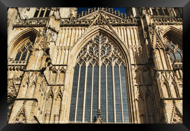 Gothic architecture detail of a cathedral's facade, featuring a large stained glass window and ornate stone carvings under clear skies in York, North Yorkshire, England. Framed Print by Man And Life