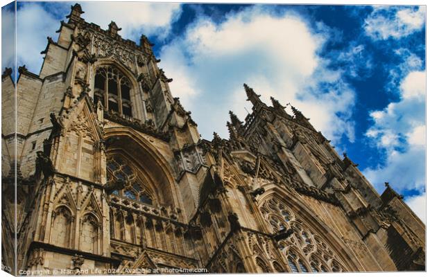 Dramatic angle of a Gothic cathedral's facade with intricate stone carvings against a vivid blue sky with fluffy clouds, showcasing architectural grandeur and historical elegance in York, North Yorkshire, England. Canvas Print by Man And Life