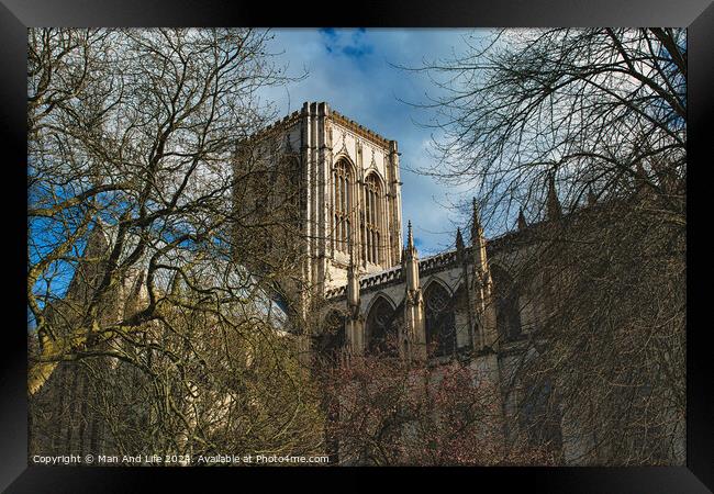 Majestic medieval cathedral with Gothic architecture, towering amidst leafless trees under a blue sky with fluffy clouds, ideal for historical or travel themes in York, North Yorkshire, England. Framed Print by Man And Life