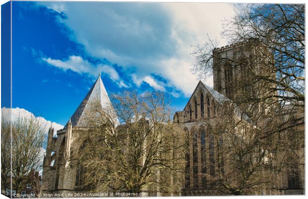 Historic medieval cathedral with Gothic architecture, featuring pointed arches and robust stone walls, set against a vibrant blue sky with fluffy clouds in York, North Yorkshire, England. Canvas Print by Man And Life