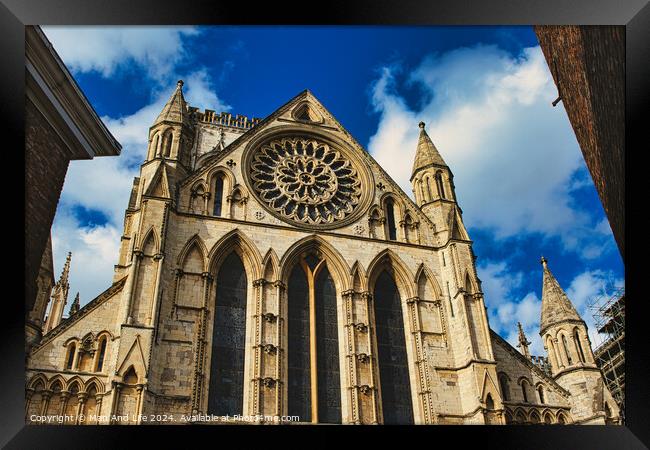 Gothic cathedral facade with rose window and spires against a blue sky with clouds, framed by trees in York, North Yorkshire, England. Framed Print by Man And Life