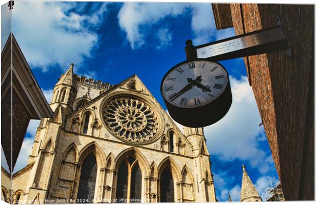 Vintage street clock hanging with a gothic cathedral facade in the background, showcasing intricate architecture and a clear blue sky in York, North Yorkshire, England. Canvas Print by Man And Life