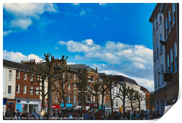 Bustling city street scene with pedestrians, unique pruned trees under a blue sky with clouds, and historic buildings, capturing the essence of urban life in York, North Yorkshire, England. Print by Man And Life