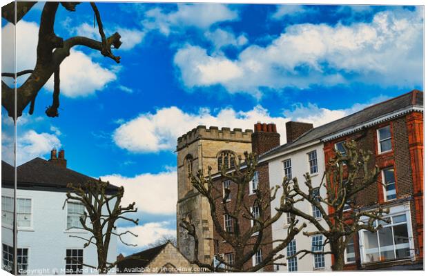 Quaint urban scene with historic stone tower, traditional buildings, and bare tree branches against a vibrant blue sky with fluffy white clouds in York, North Yorkshire, England. Canvas Print by Man And Life