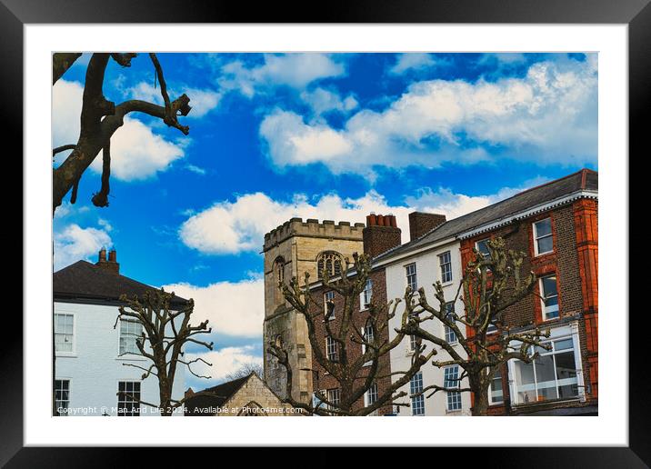 Quaint urban scene with historic stone tower, traditional buildings, and bare tree branches against a vibrant blue sky with fluffy white clouds in York, North Yorkshire, England. Framed Mounted Print by Man And Life