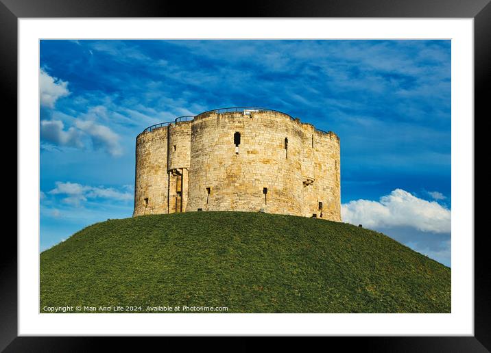 Medieval stone tower atop a lush green hill against a vibrant blue sky with fluffy clouds, symbolizing historical fortification and ancient architecture in York, North Yorkshire, England. Framed Mounted Print by Man And Life