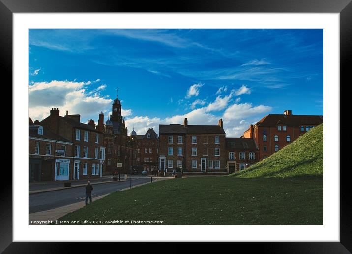 Quaint European town with historic buildings under a dramatic blue sky with fluffy clouds, featuring a lush green hill and pedestrians on a sidewalk in York, North Yorkshire, England. Framed Mounted Print by Man And Life