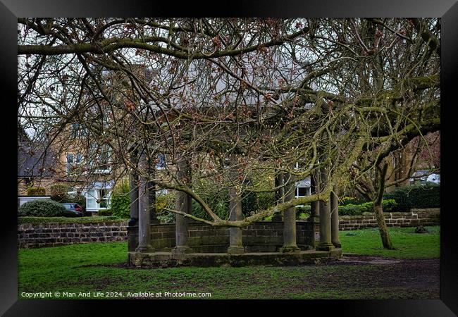 Tranquil park scene with bare-branched trees in early spring, showcasing a rustic stone bench beneath, on a carpet of green grass, with residential buildings in the background in Harrogate, North Yorkshire. Framed Print by Man And Life