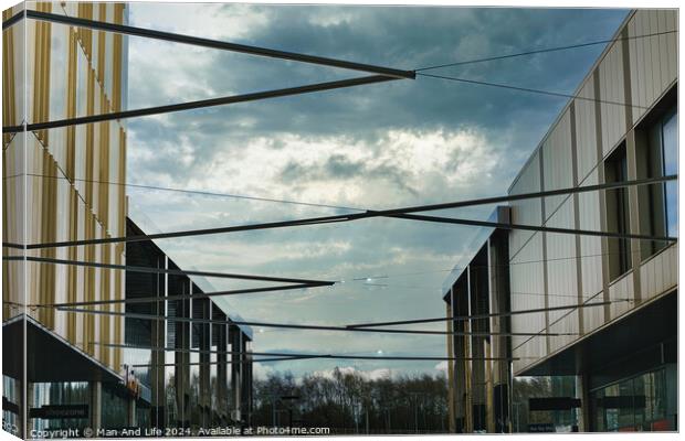 Modern architecture with geometric metal structures against a dramatic cloudy sky, showcasing contemporary urban design and open spaces. Canvas Print by Man And Life