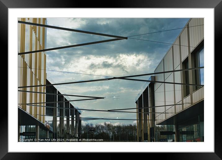 Modern architecture with geometric metal structures against a dramatic cloudy sky, showcasing contemporary urban design and open spaces. Framed Mounted Print by Man And Life