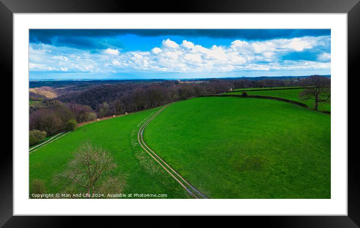 Scenic countryside landscape with lush green fields, a winding path, and a vibrant blue sky with scattered clouds. Ideal for backgrounds and nature themes. Framed Mounted Print by Man And Life