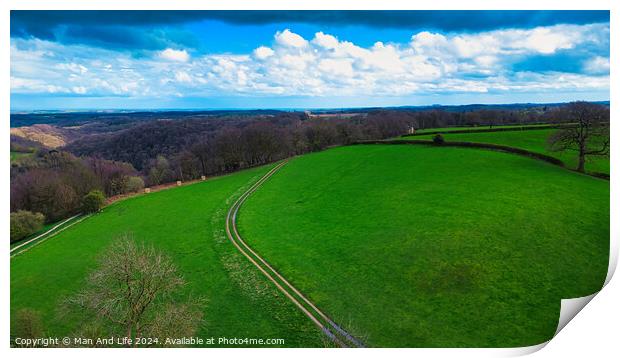Scenic countryside landscape with lush green fields, a winding path, and a vibrant blue sky with scattered clouds. Ideal for backgrounds and nature themes. Print by Man And Life