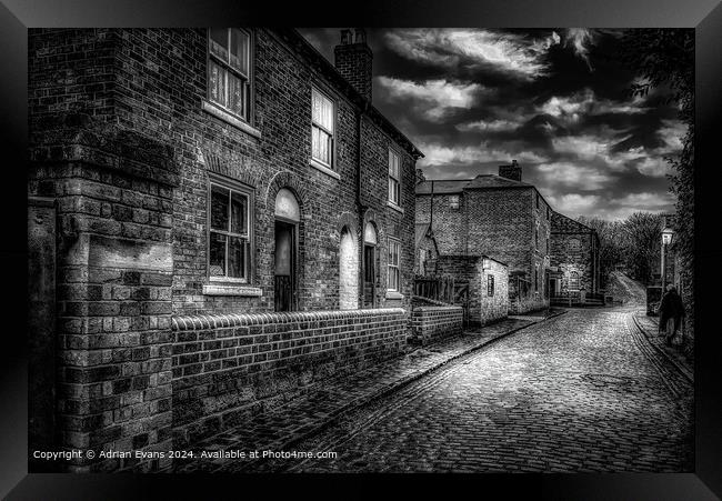 Victorian cobble stone street and shops England lit by lamps  Framed Print by Adrian Evans