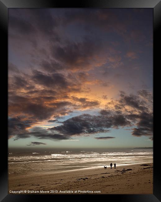 Couple walking on beach at sunset Framed Print by Graham Moore