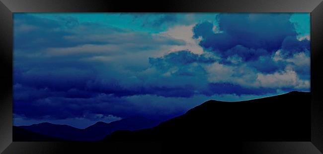 Silhouette Mountains with a stormy blue sky in Ice Framed Print by Sue Bottomley