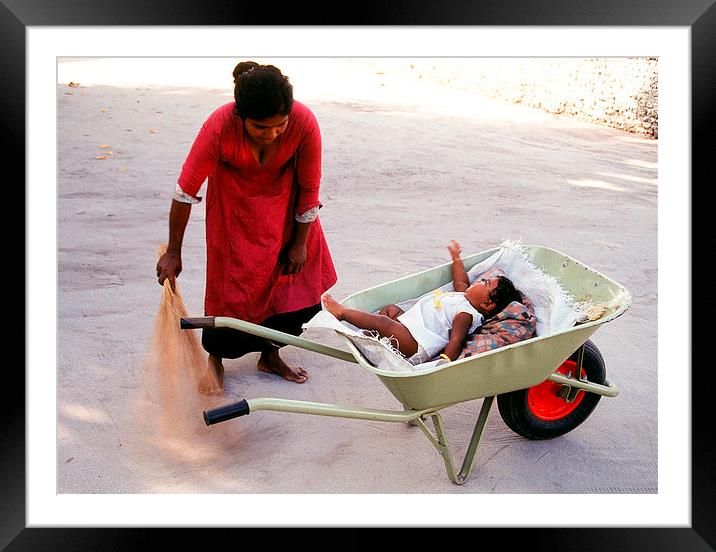  Mother keeps child in a wheel burrow while cleani Framed Mounted Print by Hassan Najmy