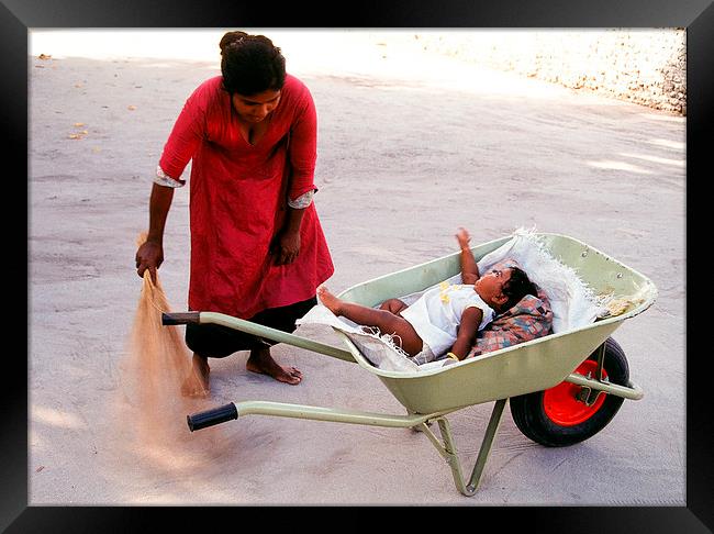  Mother keeps child in a wheel burrow while cleani Framed Print by Hassan Najmy
