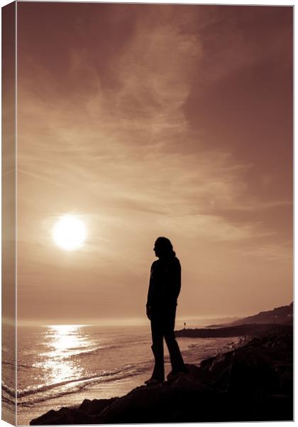 Silhouetted girl stands by sea at sunset Canvas Print by George Cairns