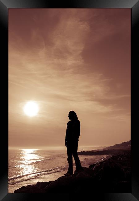 Silhouetted girl stands by sea at sunset Framed Print by George Cairns