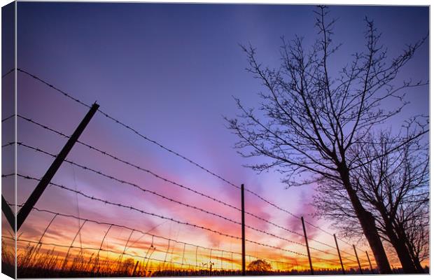 Fiery sunset viewed through barbed fence Canvas Print by Simon Bratt LRPS