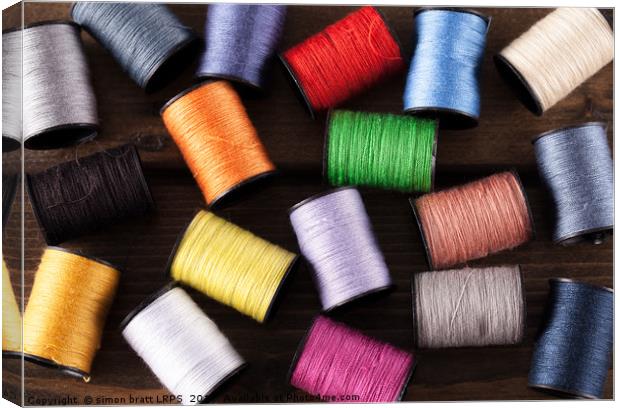Colorful cotton reels scattered on dark wood Canvas Print by Simon Bratt LRPS