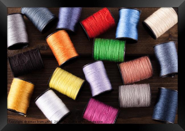 Colorful cotton reels scattered on dark wood Framed Print by Simon Bratt LRPS