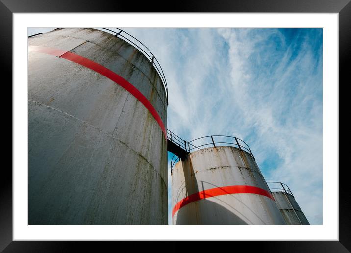 Industrial fuel tanks against a blue sky Framed Mounted Print by Tom Radford