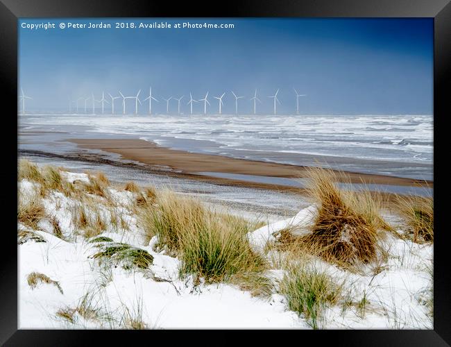 Cold conditions on a deserted beach with snowy cli Framed Print by Peter Jordan