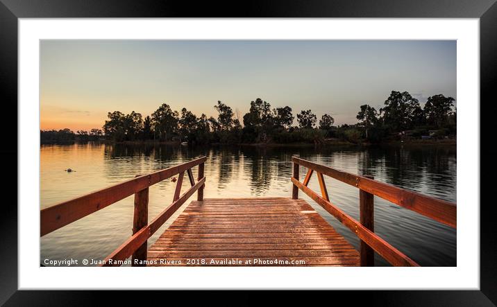Reddish wooden pier over the lake with calm waters Framed Mounted Print by Juan Ramón Ramos Rivero