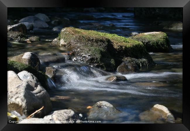 Water flowing over a rock Framed Print by Connor Carter
