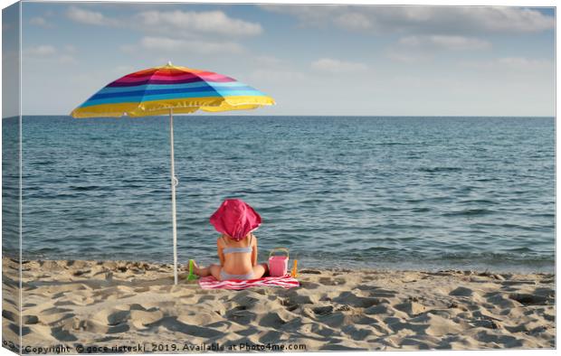 little girl with hat sitting under sunshade on bea Canvas Print by goce risteski