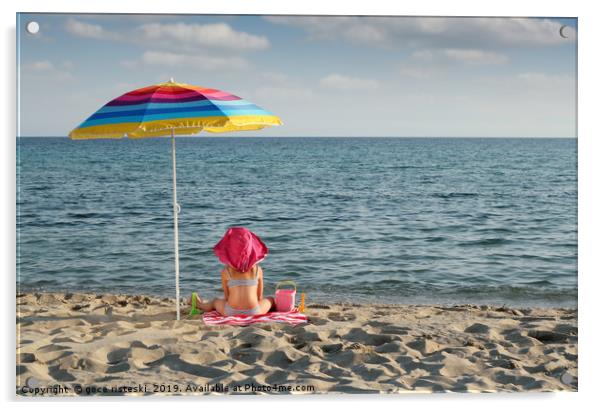 little girl with hat sitting under sunshade on bea Acrylic by goce risteski