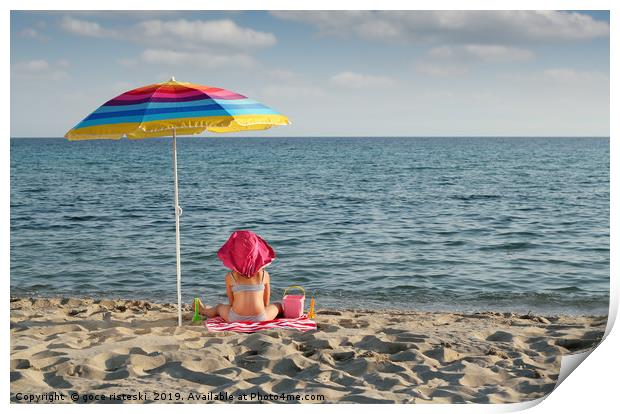little girl with hat sitting under sunshade on bea Print by goce risteski