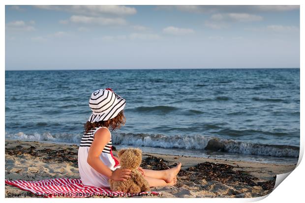 little girl with teddy bear sitting on beach Print by goce risteski
