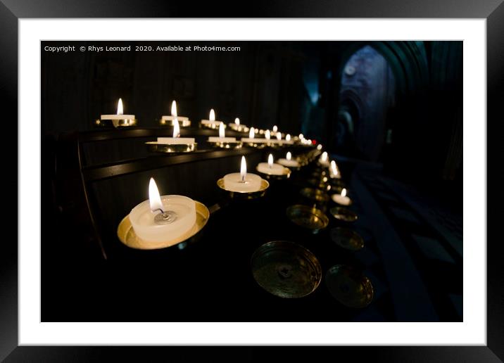 Prayer candles shine bright in a dark cathedral Framed Mounted Print by Rhys Leonard