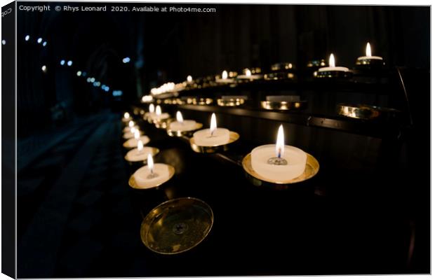 Prayer candles shine bright in a dark cathedral Canvas Print by Rhys Leonard