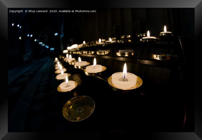Prayer candles shine bright in a dark cathedral Framed Print by Rhys Leonard