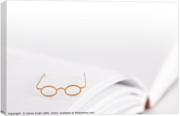 Tiny reading glasses on open book Canvas Print by Simon Bratt LRPS