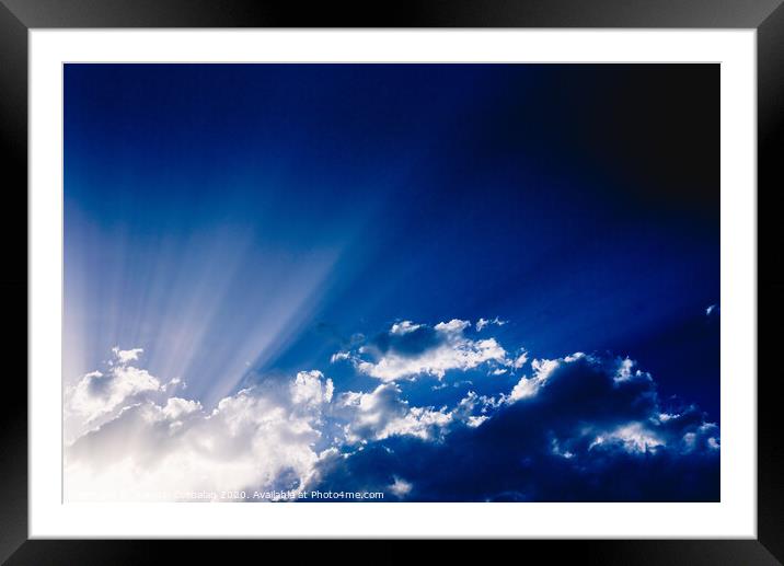 Sunbeams rising from a large cloud in intense blue sky on a summer afternoon Framed Mounted Print by Joaquin Corbalan
