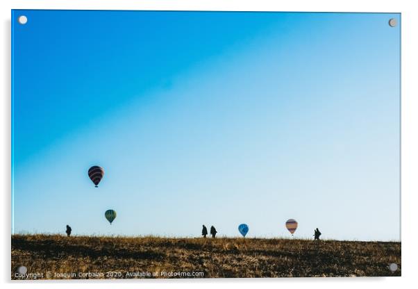 Silhouettes of tourists walking through a meadow while watching hot air balloons flying on the horizon, blue sky background, copy space, added film grain. Acrylic by Joaquin Corbalan
