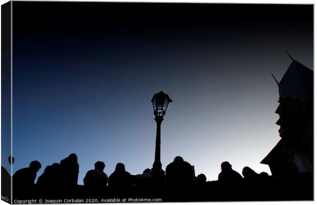  A crowd of tourists rests at dusk on a bridge, silhouetted images backlight against a streetlight. Canvas Print by Joaquin Corbalan