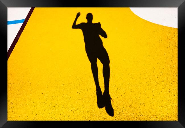 Shadow and silhouette of a man jumping on a yellow painted floor. Framed Print by Joaquin Corbalan