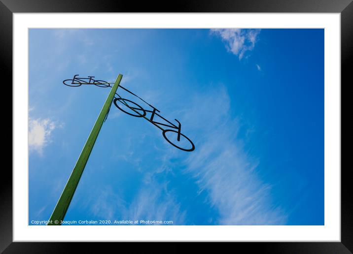 Post with the figure of some bicycles indicating the road, with blue sky and clouds in the background. Framed Mounted Print by Joaquin Corbalan