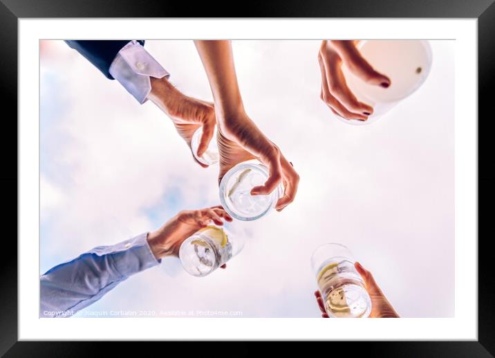 Group of friends toasting with a few glasses of alcohol with the sky in the background, seen from below. Framed Mounted Print by Joaquin Corbalan