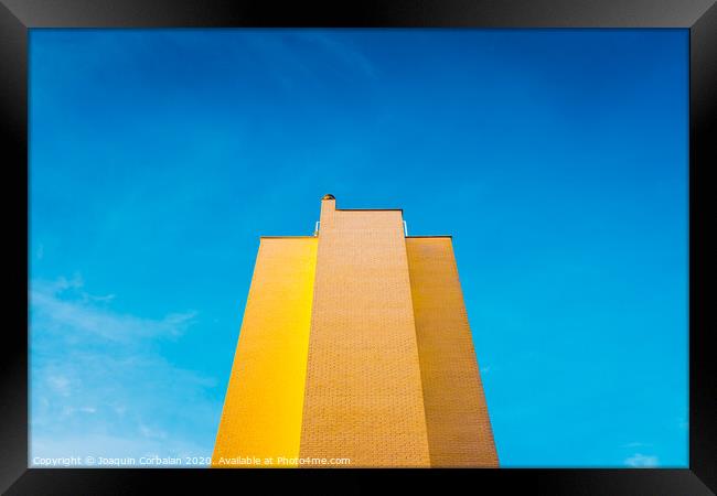 High brick building, warm and yellow at sunset, with the background of an intense blue sky and copy space, minimalist architecture. Framed Print by Joaquin Corbalan