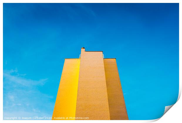 High brick building, warm and yellow at sunset, with the background of an intense blue sky and copy space, minimalist architecture. Print by Joaquin Corbalan
