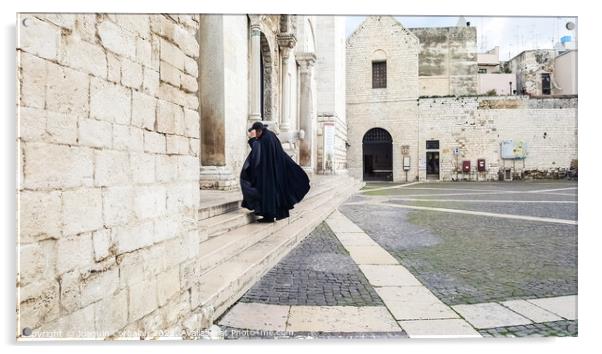 Bari, Italy - March 12, 2019: A Catholic priest walks towards the cathedral dressed in a black cape and hat a day of wind and rain. Acrylic by Joaquin Corbalan
