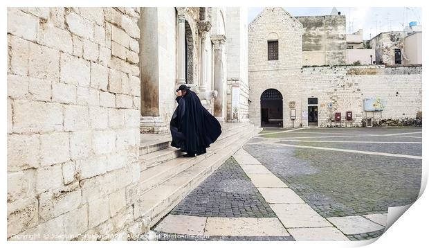 Bari, Italy - March 12, 2019: A Catholic priest walks towards the cathedral dressed in a black cape and hat a day of wind and rain. Print by Joaquin Corbalan